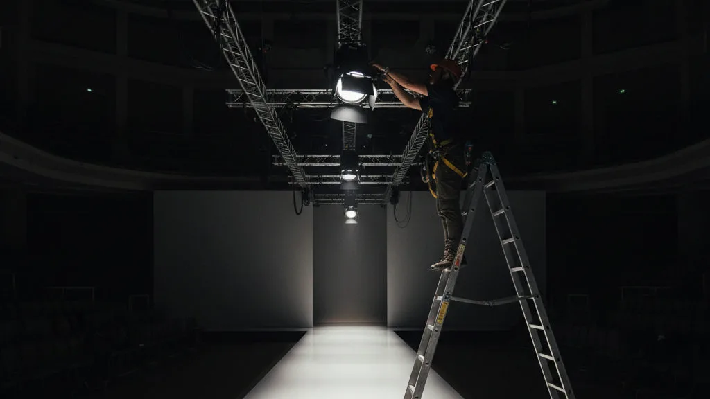 Technician focusing a lighting fixture on truss above an empty lit runway
